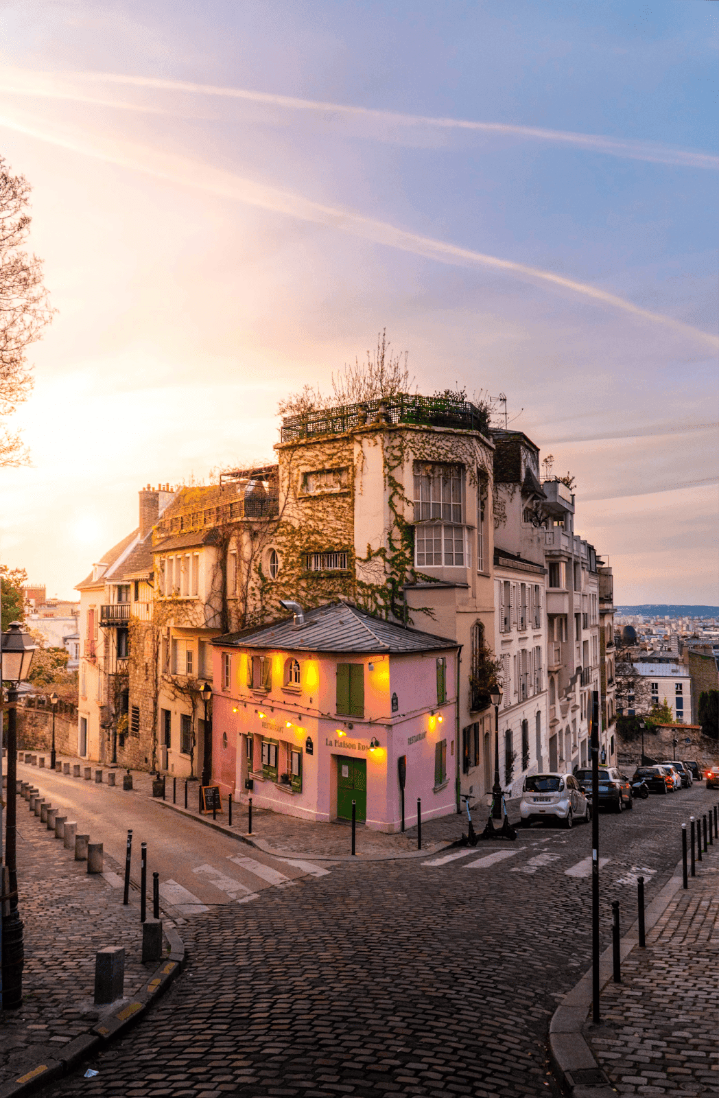 A charming street corner in Montmartre, Paris, with ivy-covered buildings, cobblestone streets, and a warm sunset sky.