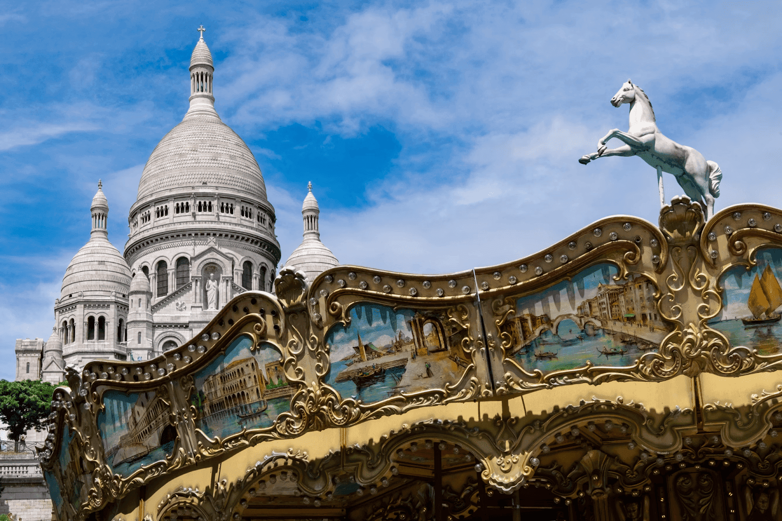 Carousel with ornate details and horse figure in front of the Sacré-Cœur Basilica under a blue sky.