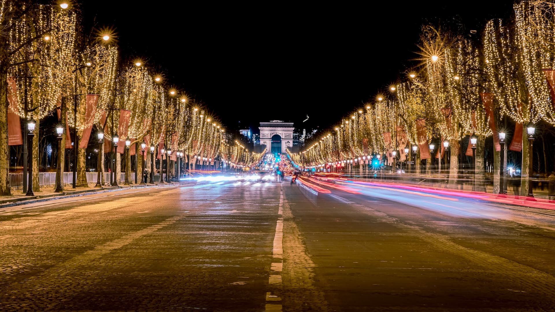 Illuminated Champs-Élysées at night with the Arc de Triomphe in the distance, lined with trees adorned with festive lights.